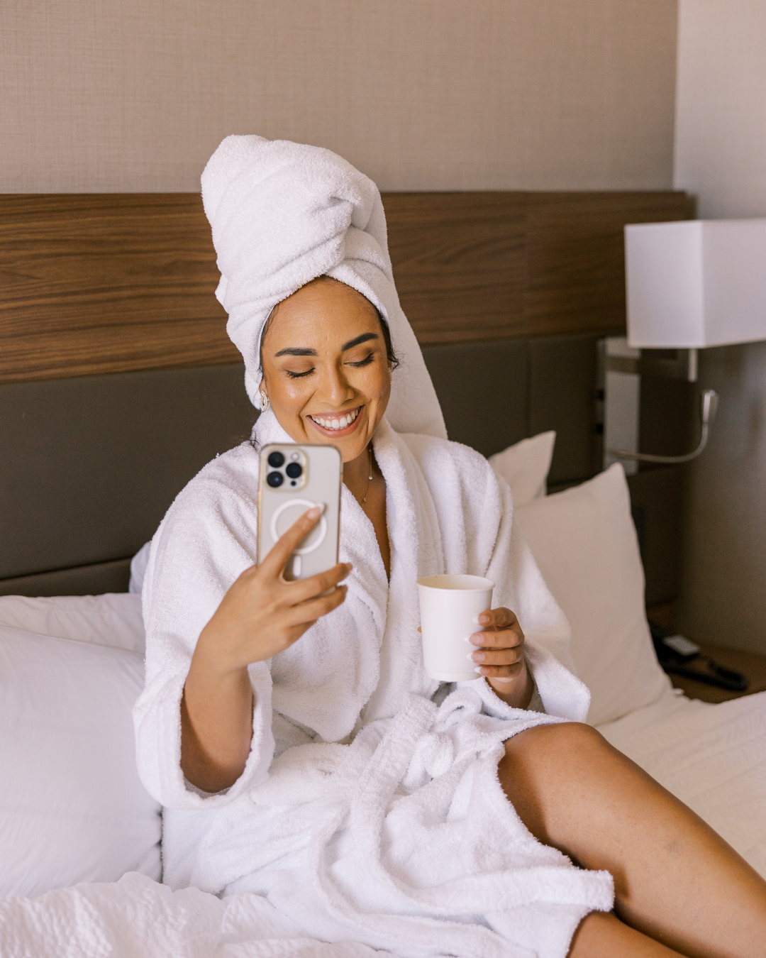 mulher feliz de roupão sentada na cama do quarto de hotel